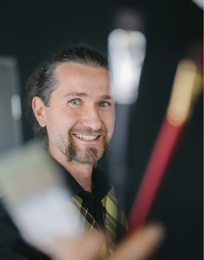 Stefan hält lächelnd Pinsel in die Kamera